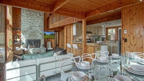 Interior acogedor de una cabaña con chimenea de piedra, comedor para cuatro personas y cocina con armarios de madera.