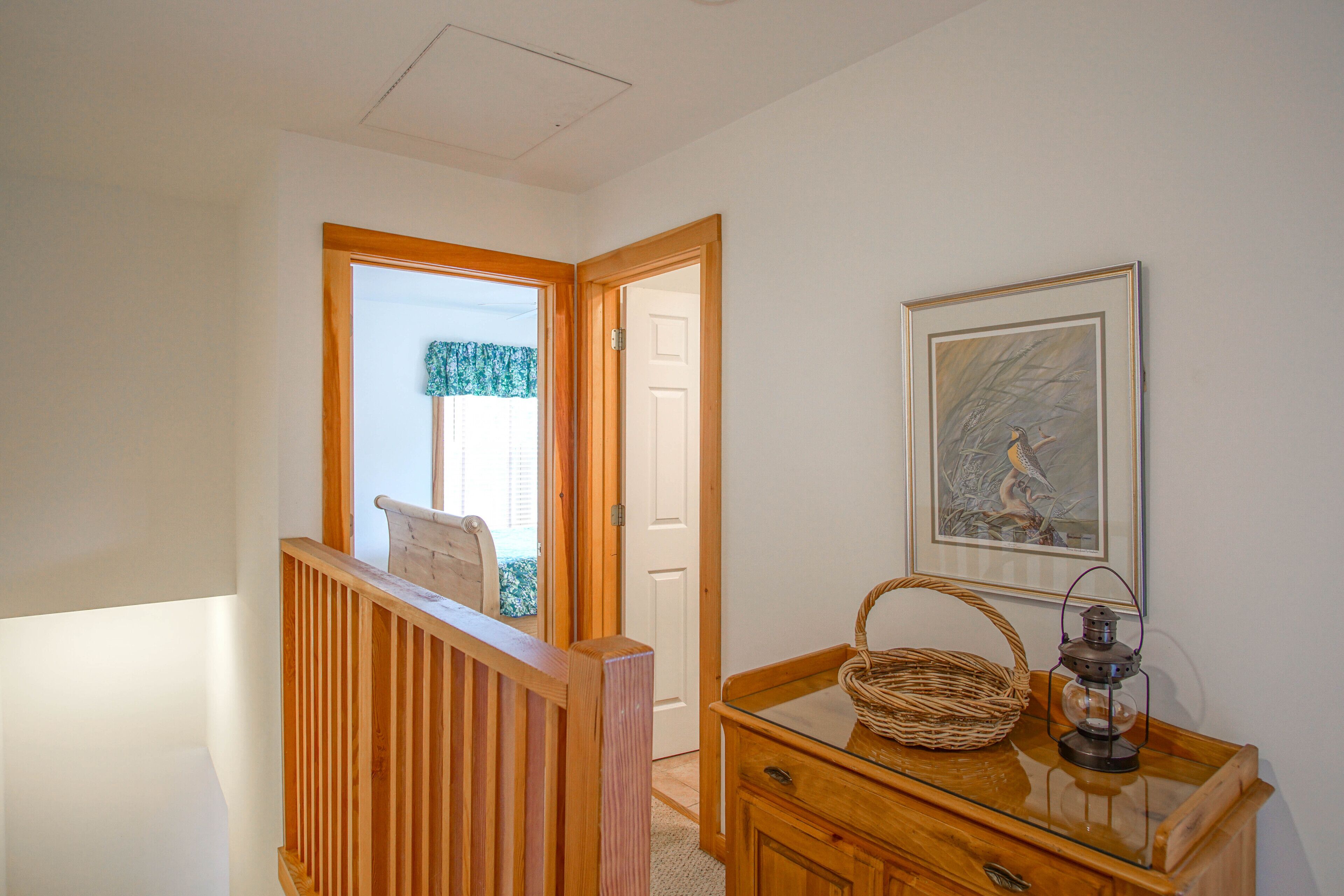 A hallway with a wooden railing, a wicker basket on a glass table, and a framed picture on the wall.
