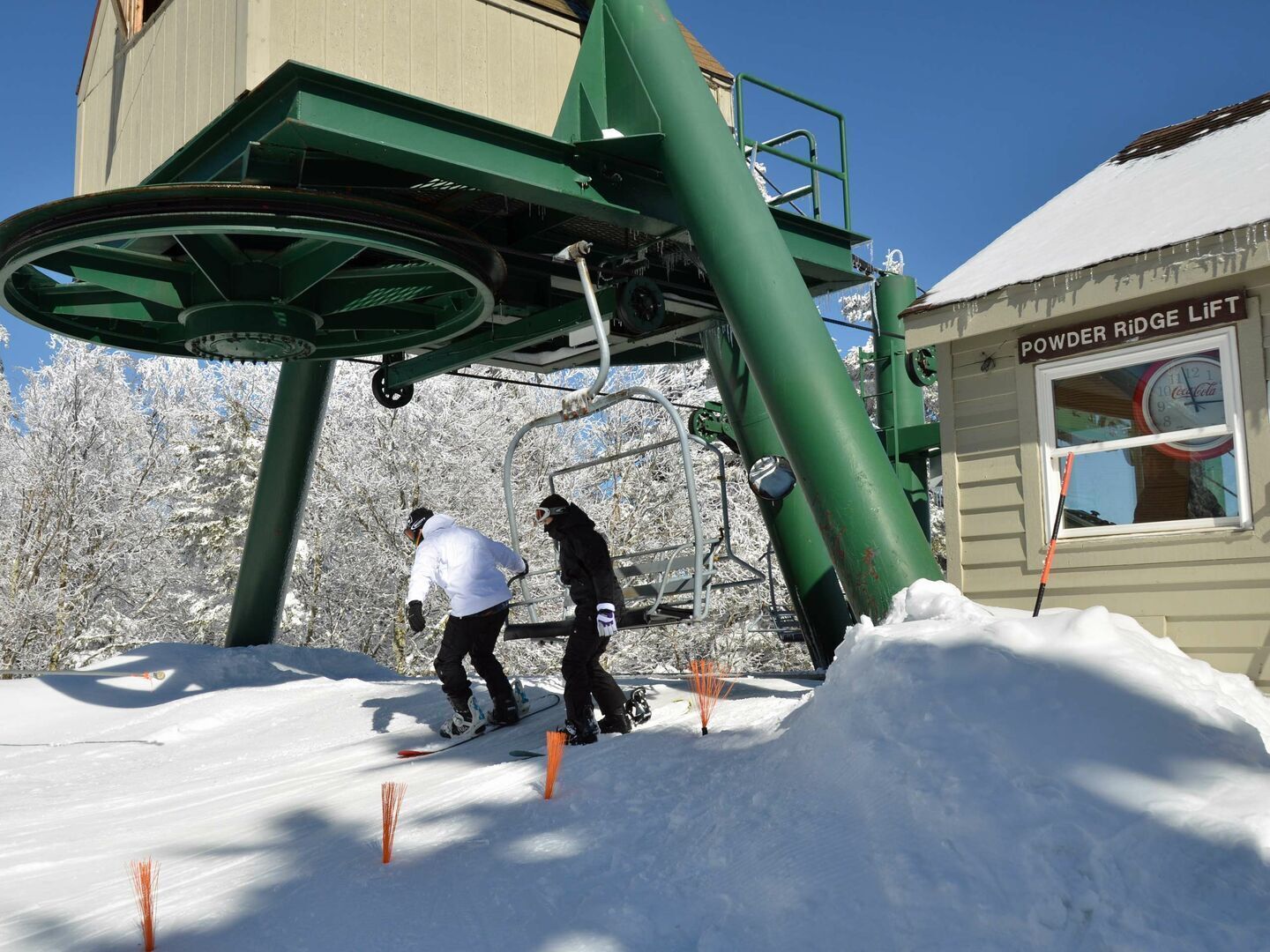 A ski lift with two people on it, surrounded by snow and trees.