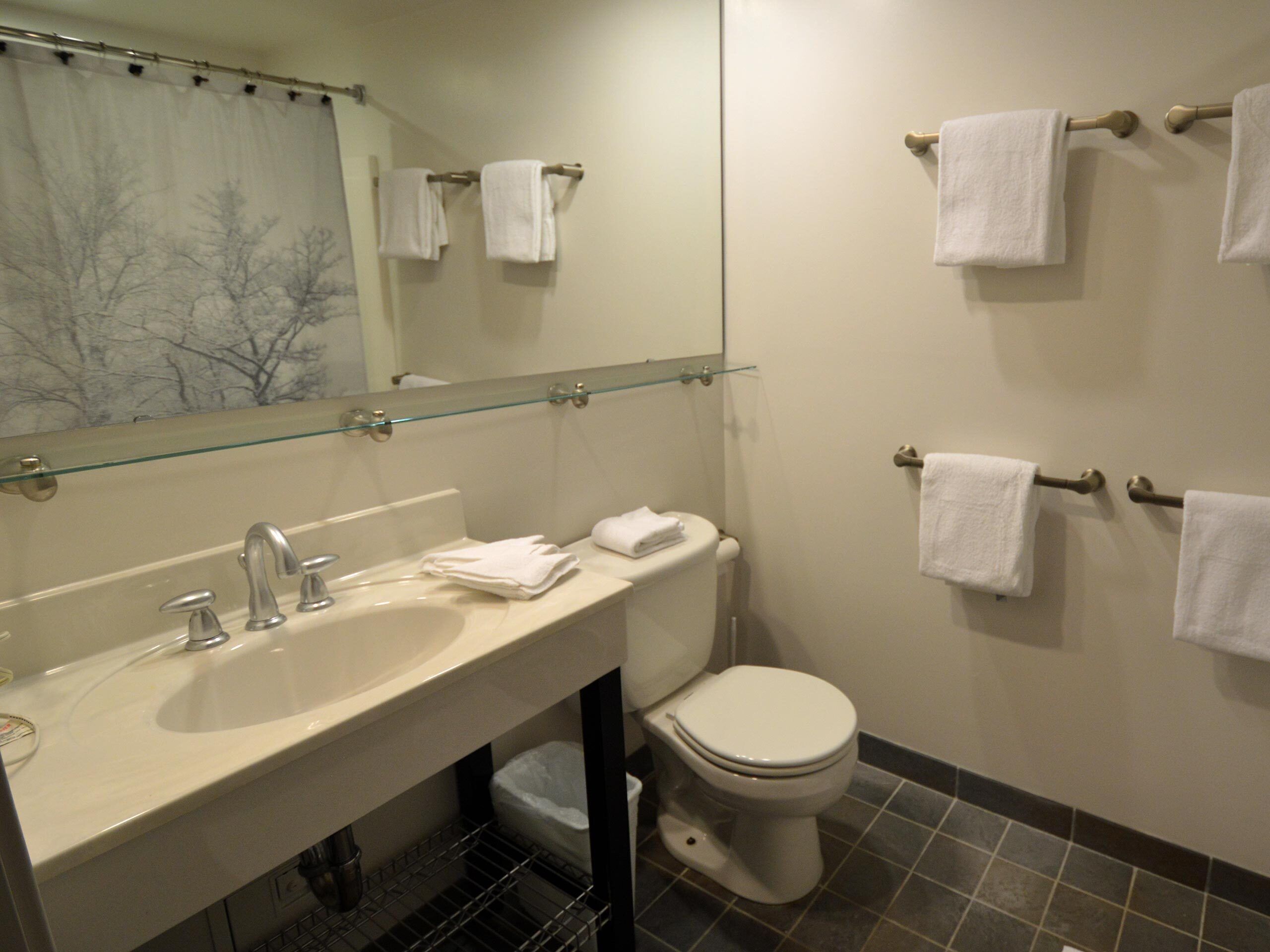A bathroom with a glass shower enclosure, a sink, a toilet, and multiple towels hanging on towel bars.