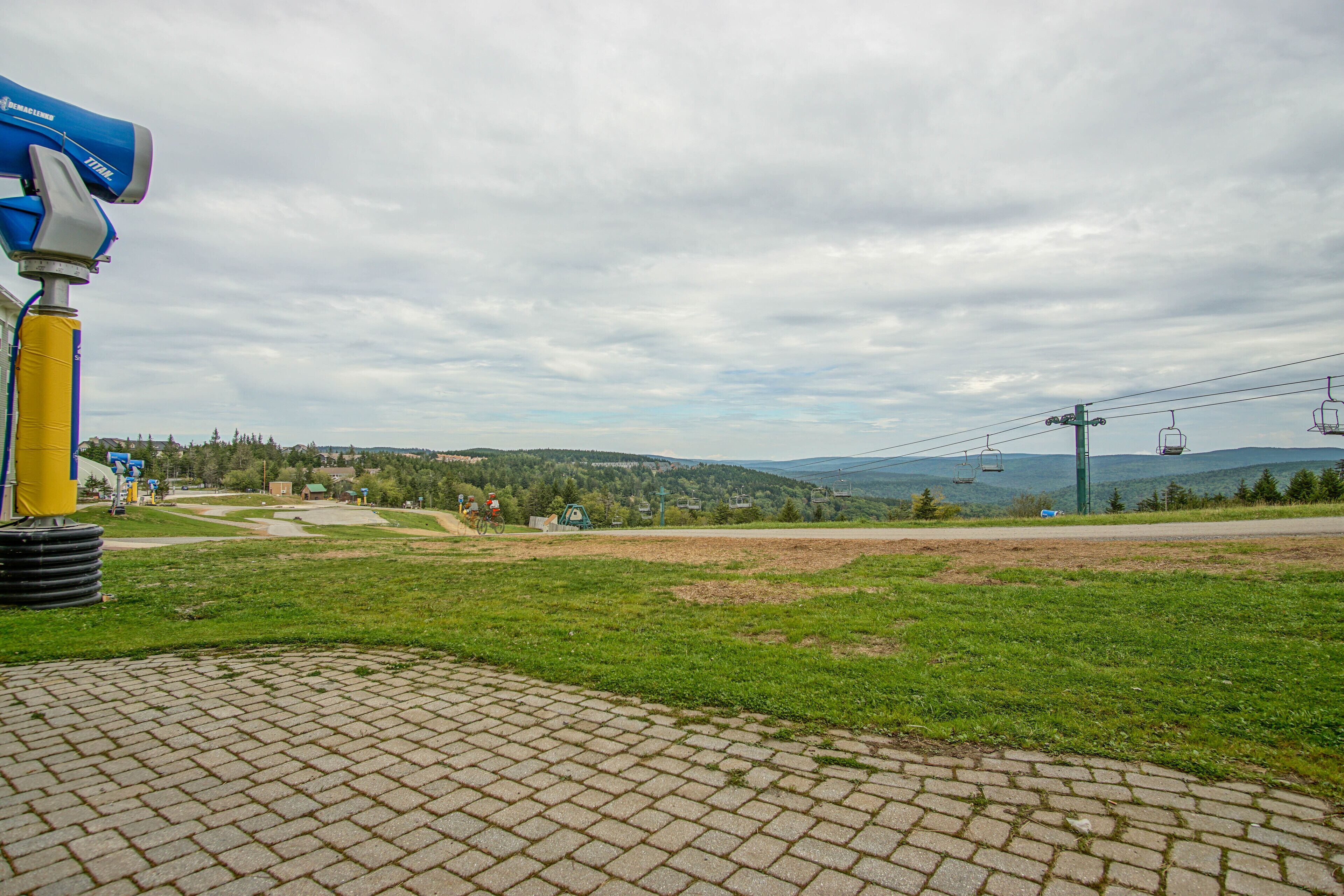 A paved area with a blue and yellow object, a grassy field, and a distant view of a mountain with a ski lift.