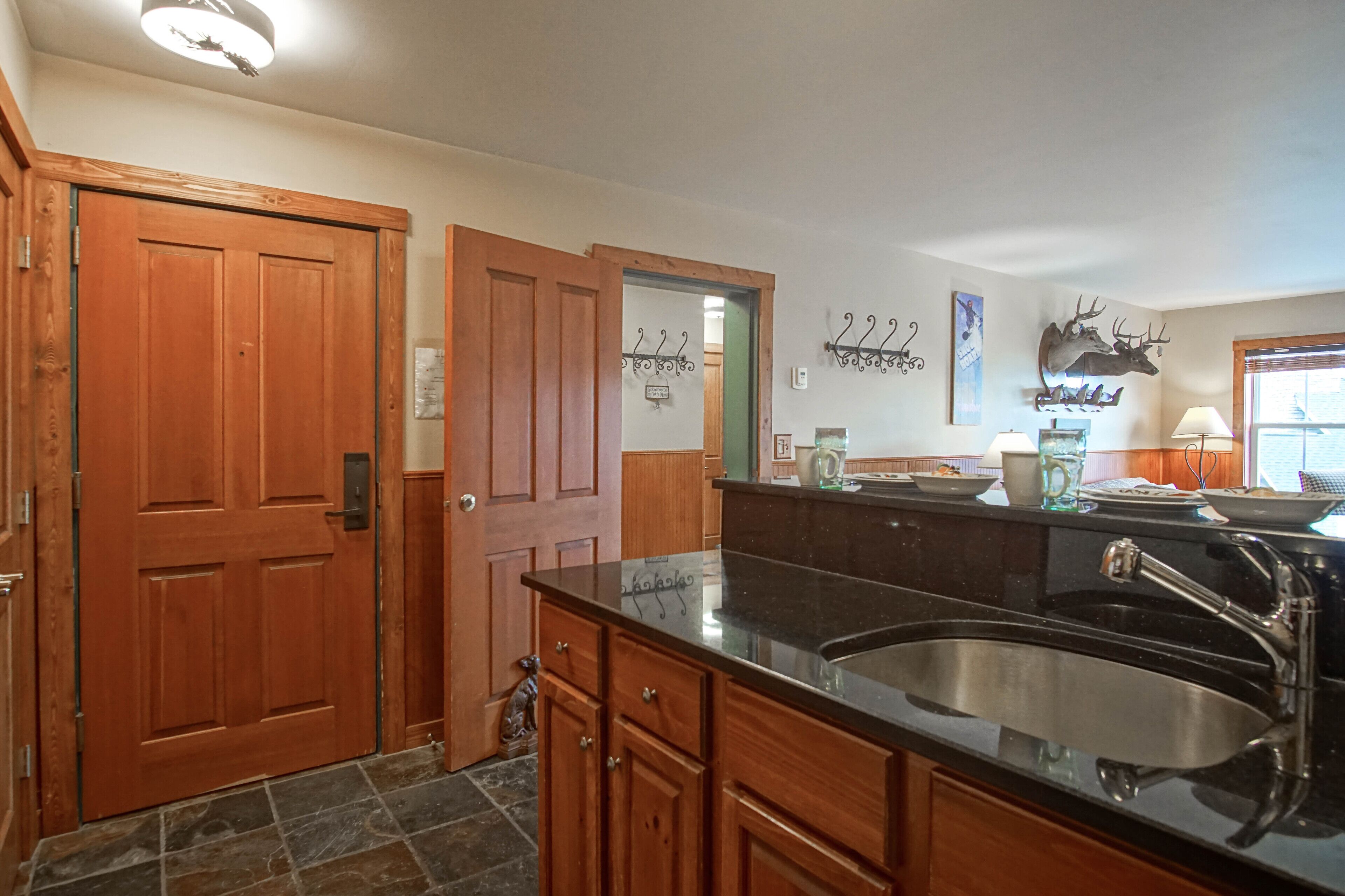 A kitchen with wooden cabinets, a black countertop, a stainless steel sink, and a deer head decoration on the wall.