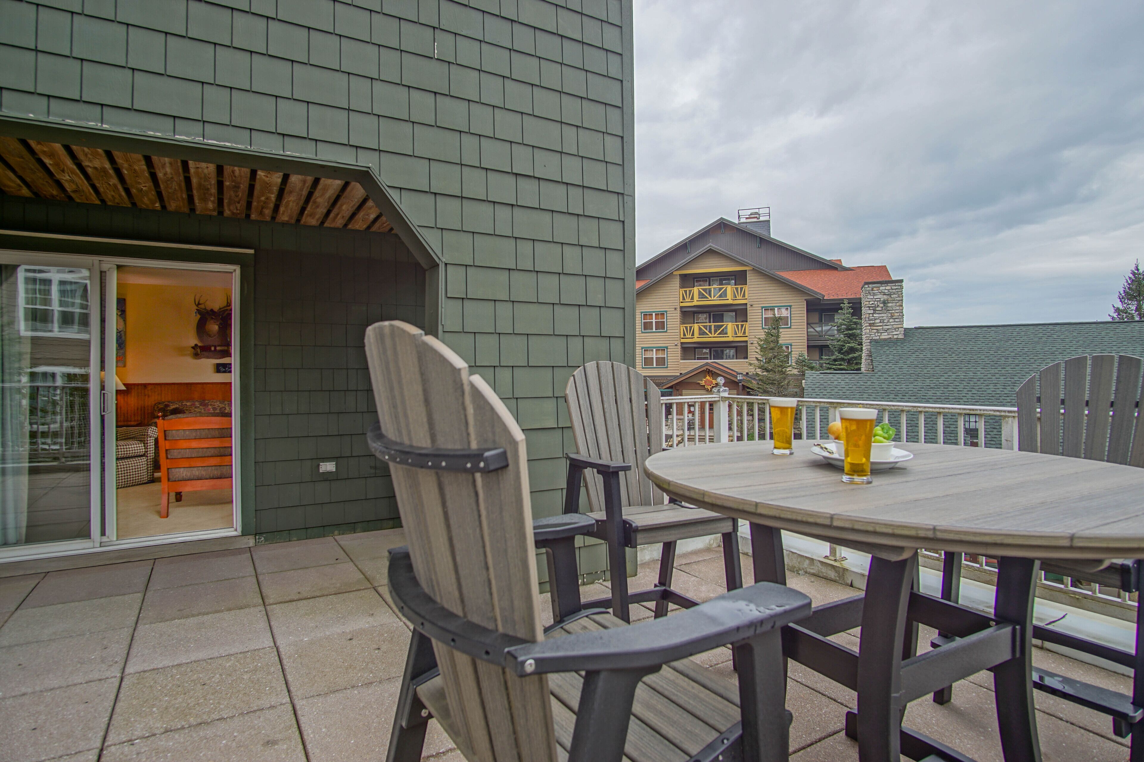 A patio with a round table and chairs, a glass door leading to a room, and a building with a stone facade in the background.