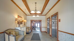 A hotel lobby with a sofa, a lamp, a chandelier, and an elevator. - Highland House #102-104: 2br: 2 Bath (Snowshoe)