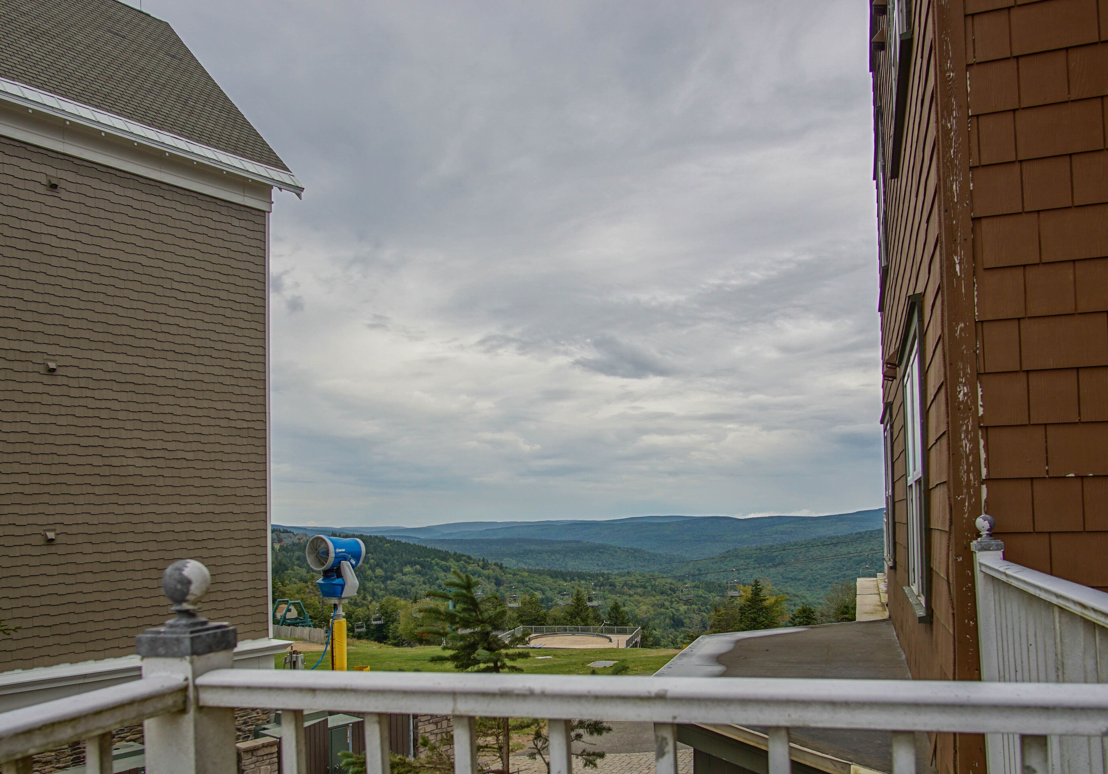 A balcony with a view of a hilly landscape, a telescope, and a building with a brick facade.