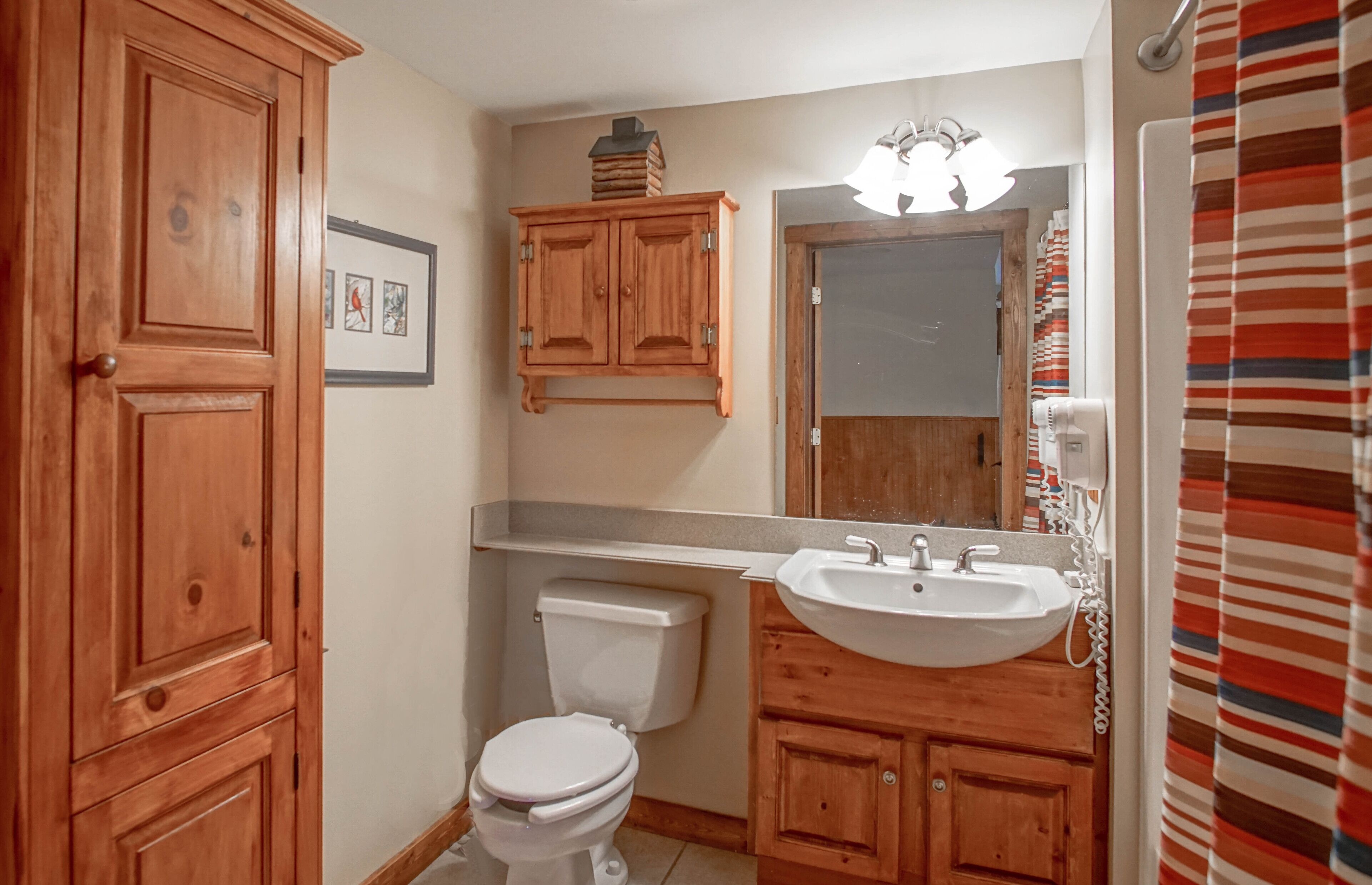 Een badkamer met houten kastjes, een toilet, een wastafel en een spiegel.