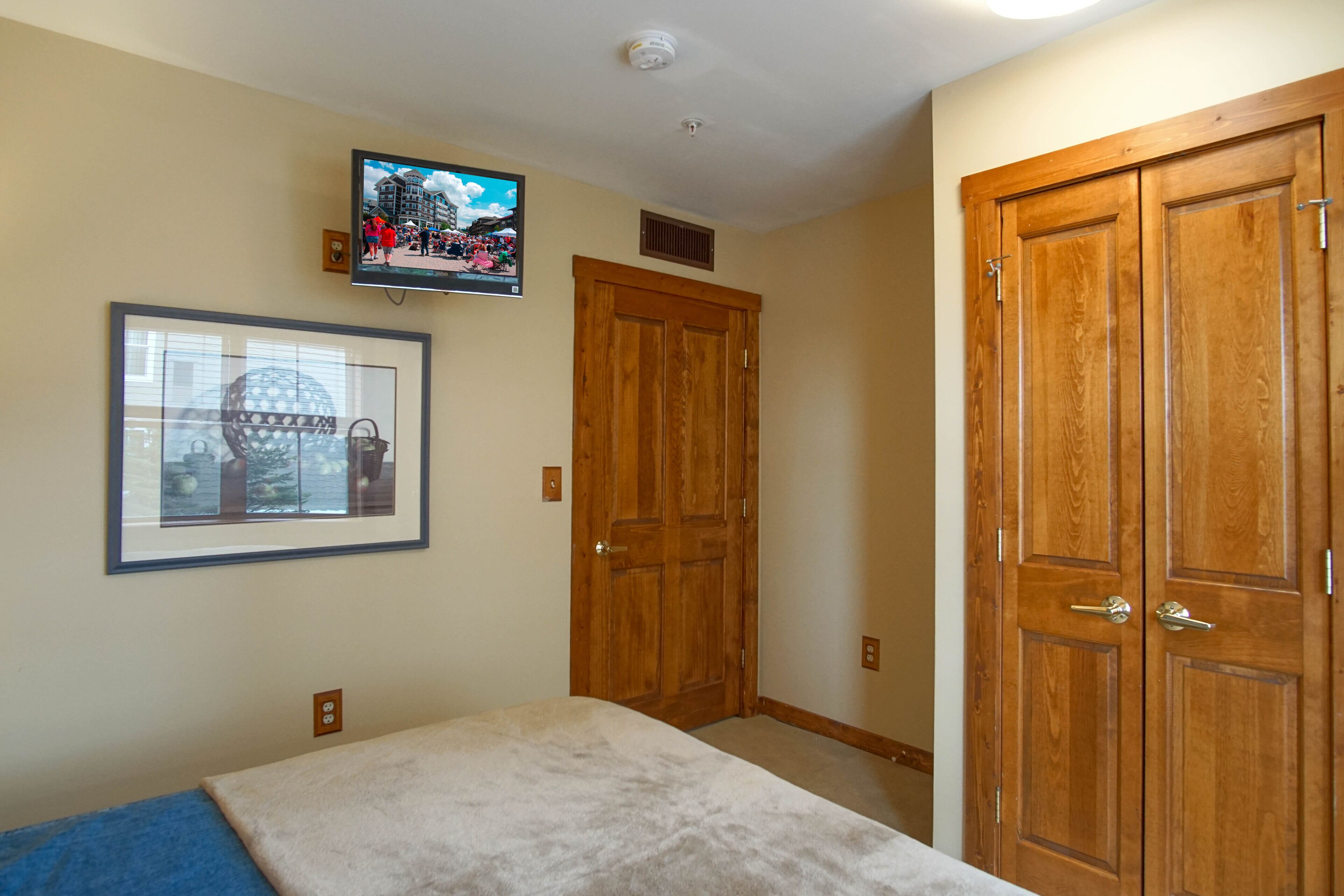 A bedroom with a bed, a television mounted on the wall, and a wooden wardrobe.