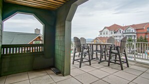 A covered outdoor area with a view of buildings and a balcony with chairs and a table. - Highland House #102-104: 2br: 2 Bath (Snowshoe)