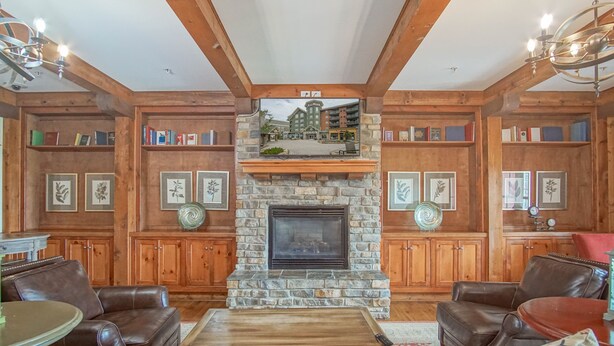 A cozy living room with a stone fireplace, leather sofas, wooden bookshelves, and a chandelier. - Highland House #102-104: 2br: 2 Bath (Snowshoe)