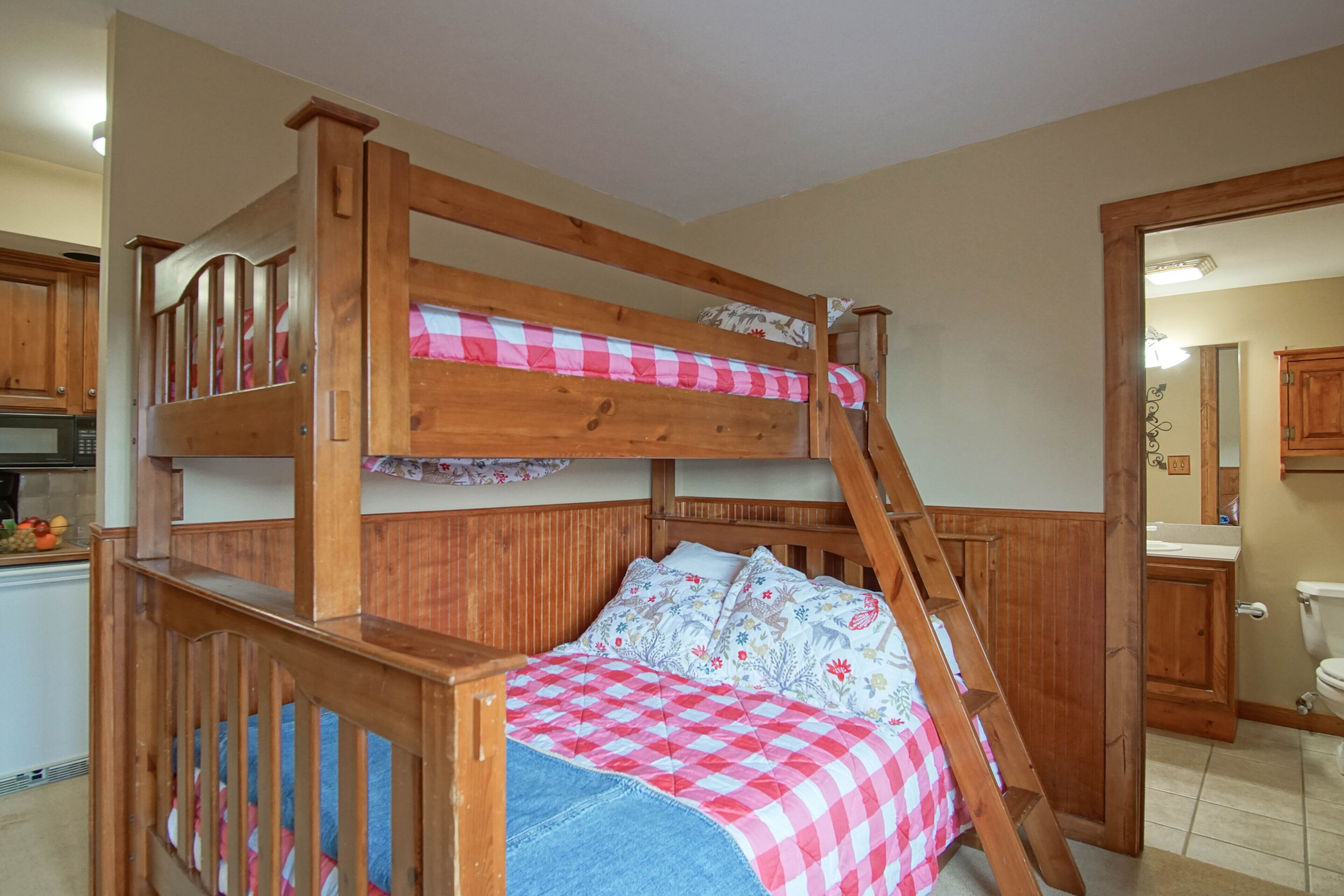 Una cama litera con escalera de madera, colcha a cuadros y almohada estampada.