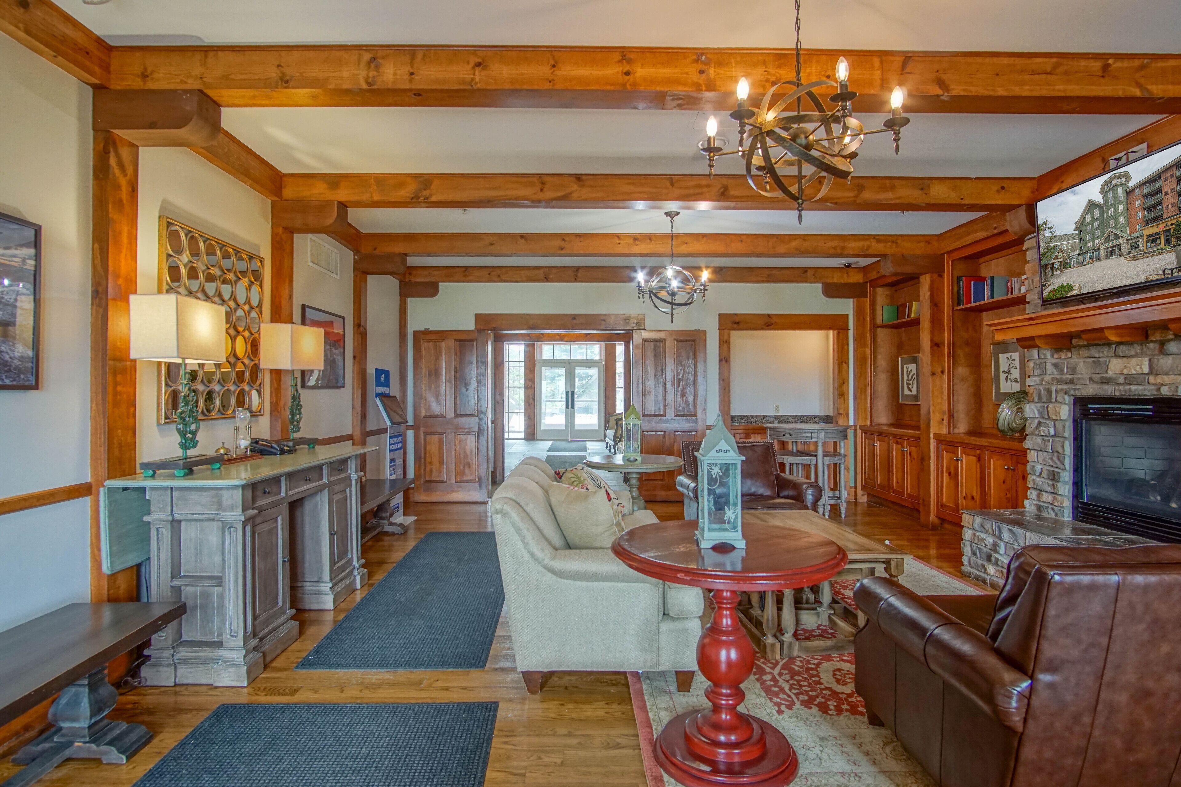 A spacious living area with wooden beams, a fireplace, a television, and a cozy seating arrangement.