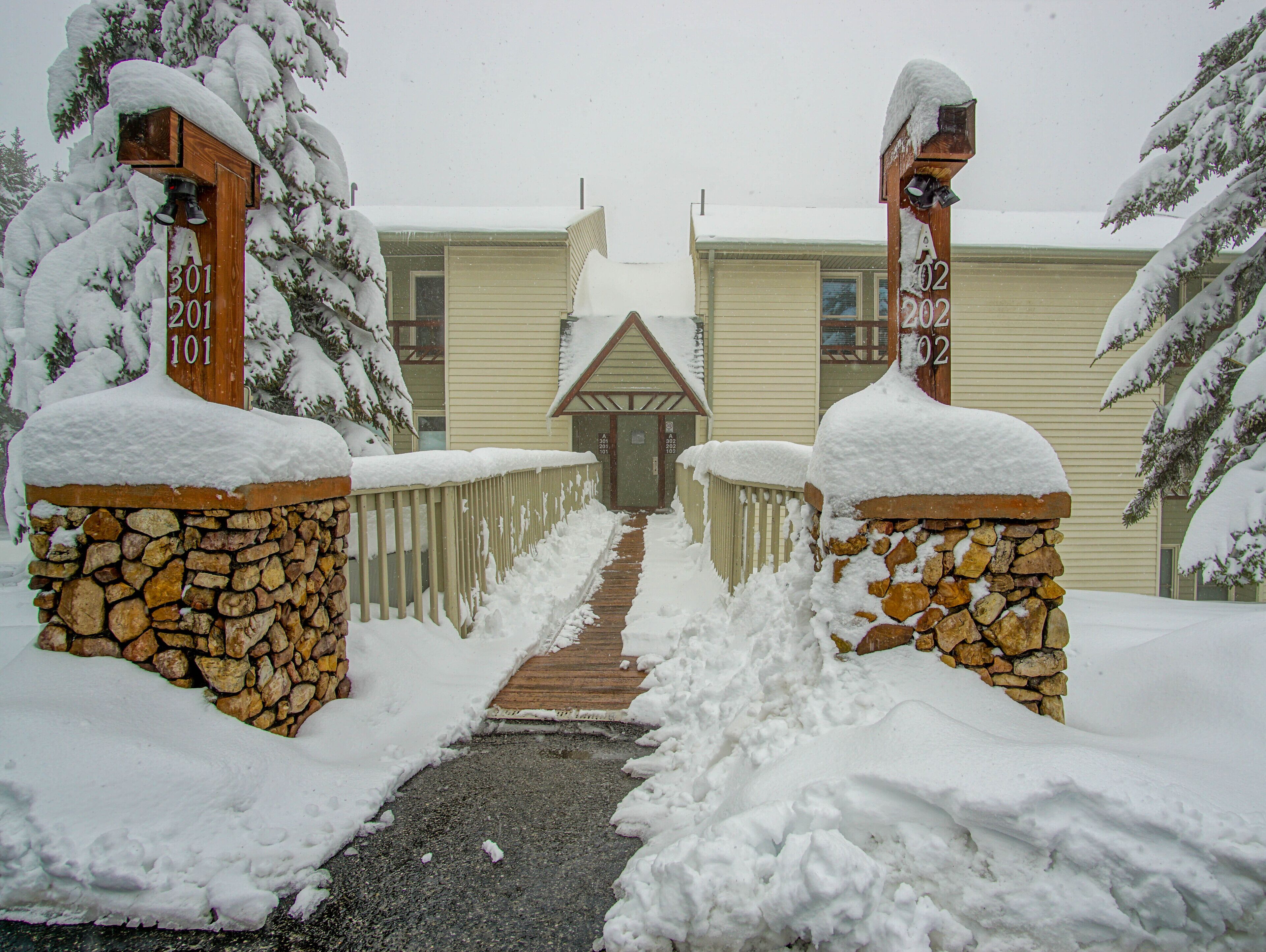 A snow-covered pathway leading to a building with stone pillars and a wooden fence.