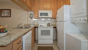 A kitchen with wooden cabinets, a white microwave, a stove, a dishwasher, and a refrigerator. - Leatherbark - 202a 2 BR Condo Spacious Living Room (Snowshoe)
