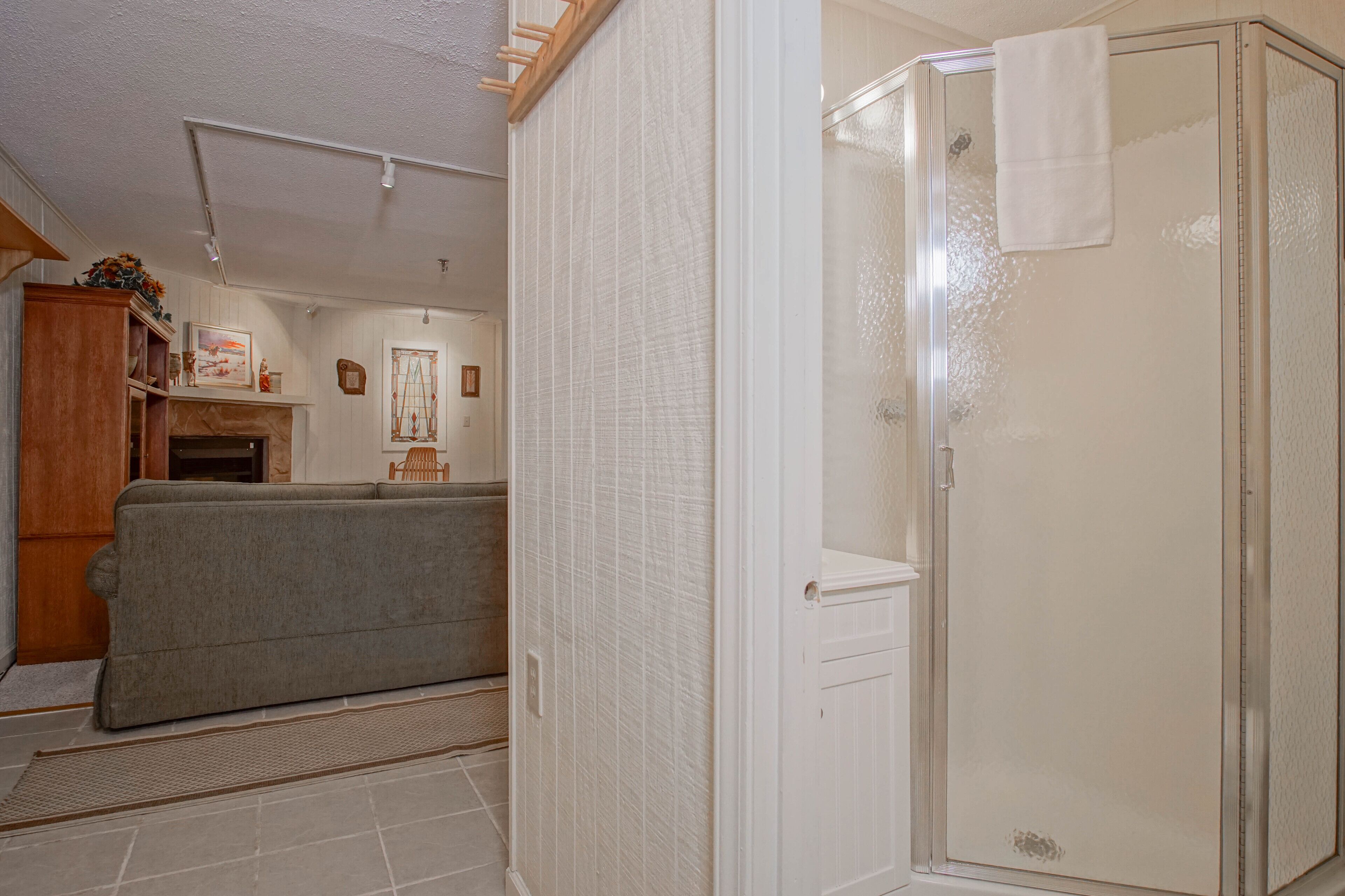 A bathroom with a glass shower enclosure, a white towel hanging on the door, and a beige floor.