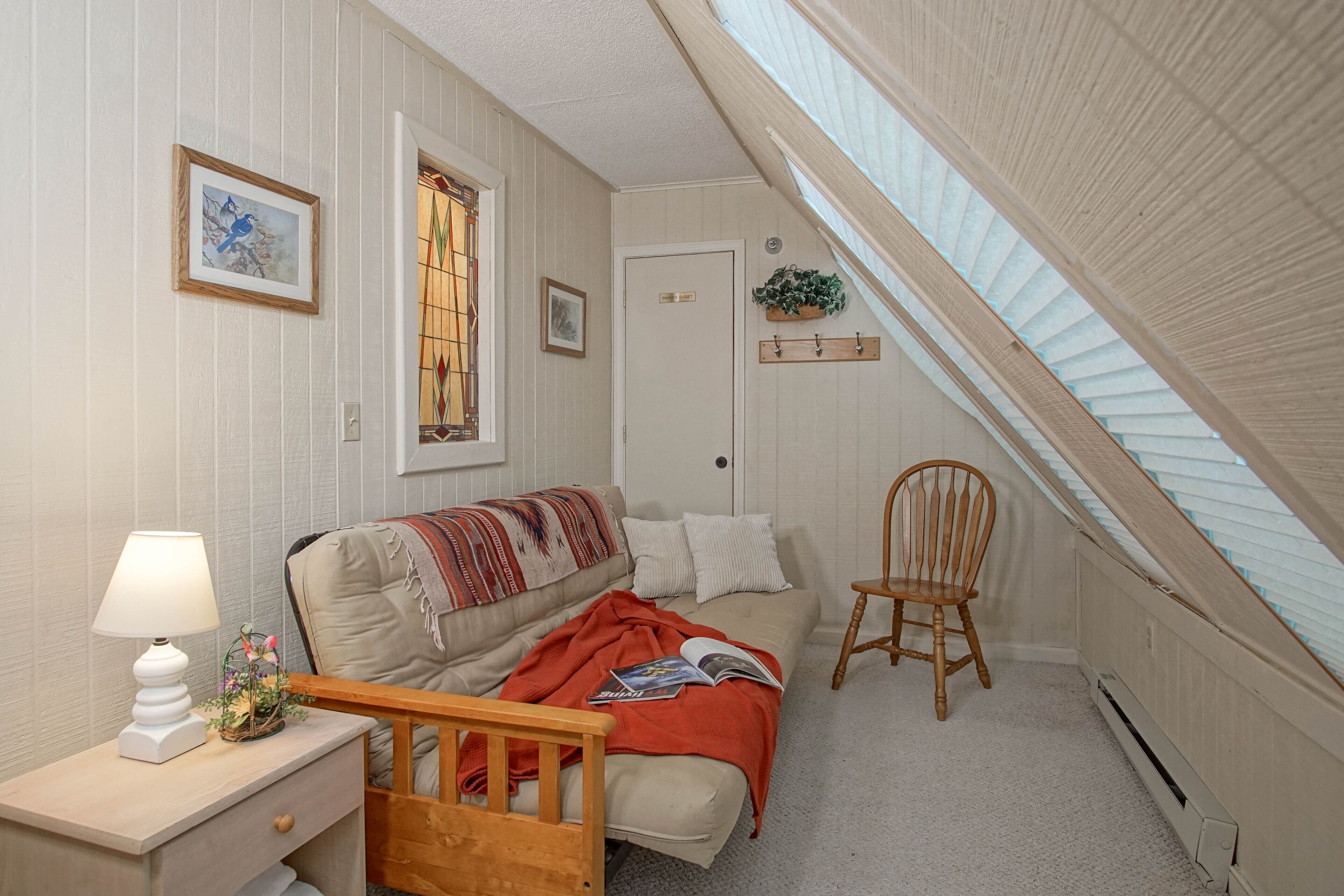 A cozy bedroom with a bed, bedside table, lamp, and a window with a view.