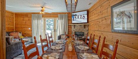 A dining area with a long wooden table set for a meal, surrounded by wooden chairs.