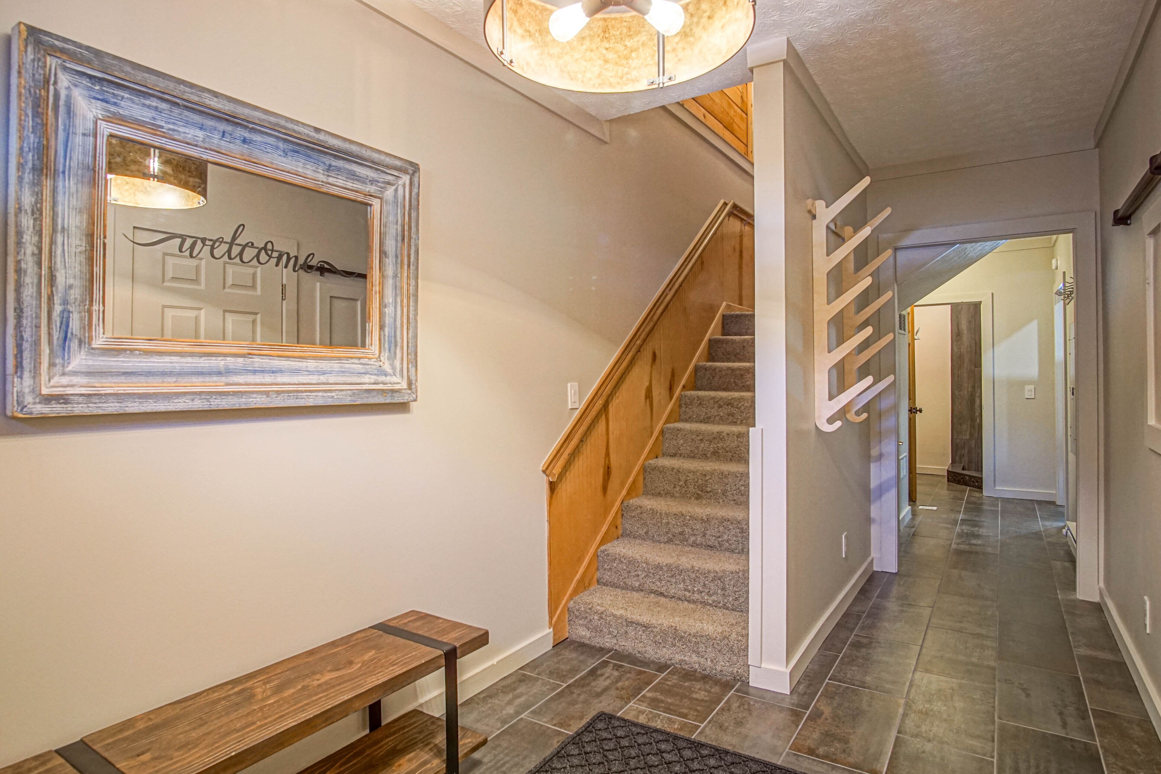 A staircase with wooden steps and a handrail, a bench, and a wall-mounted mirror with a 'welcome' sign.