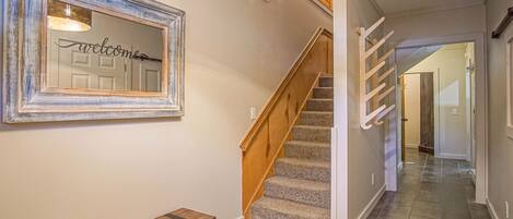 A staircase with wooden steps and a handrail, a bench, and a wall-mounted mirror with a 'welcome' sign.