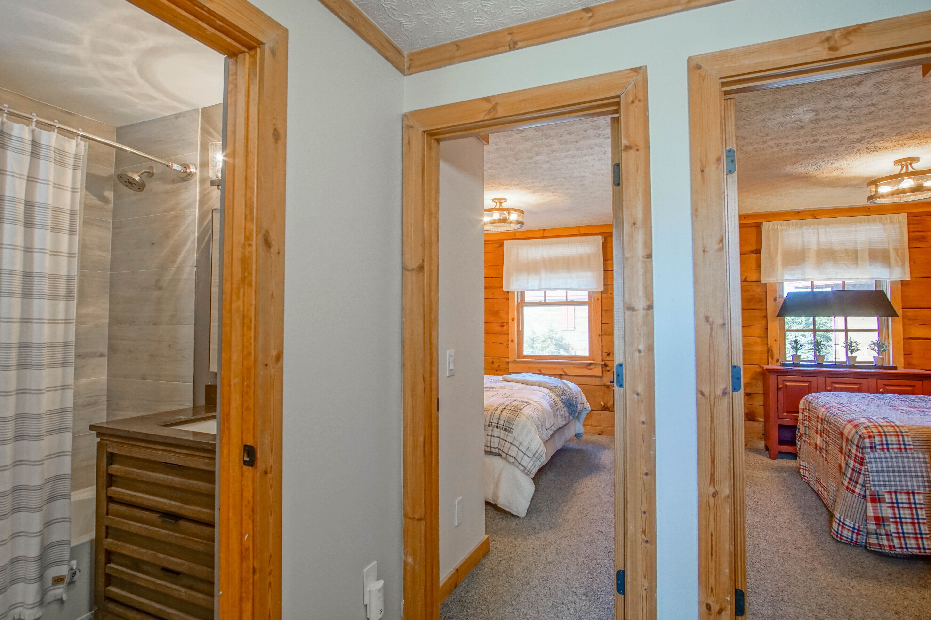 A bedroom with a wooden door, a bed with a plaid duvet, a wooden dresser, and a window with a white blind.