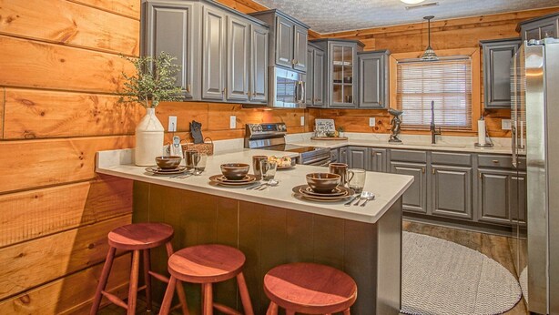 Una cocina con paneles de madera, una isla central con taburetes, un refrigerador y una estufa.