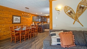 Interior acogedor de una cabaña con comedor, cocina y sala de estar con sofá y decoración en las paredes.