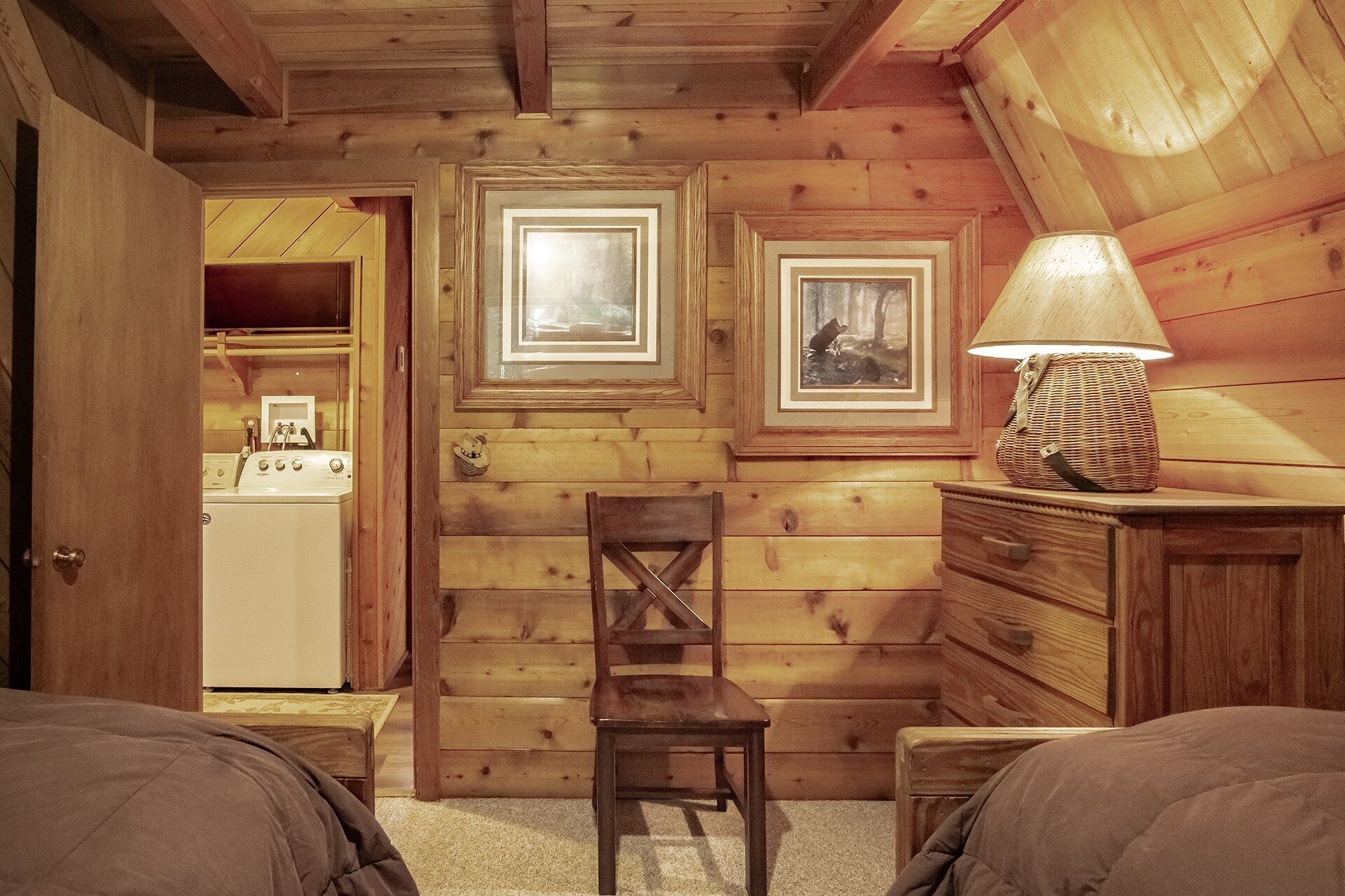 A cozy cabin room with wooden walls, a wooden chair, a dresser, and a lamp.