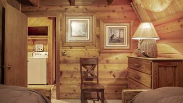 A cozy cabin room with wooden walls, a wooden chair, a dresser, and a lamp.