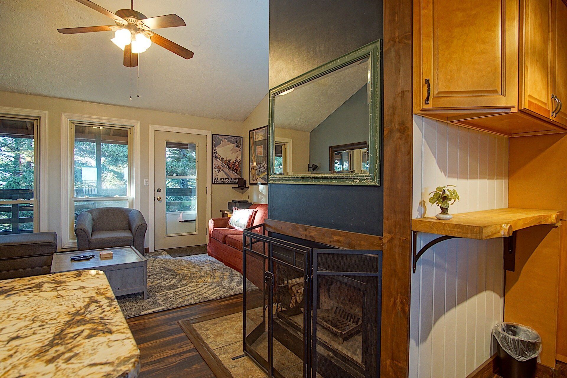 A cozy living room with a fireplace, a ceiling fan, and a large mirror.