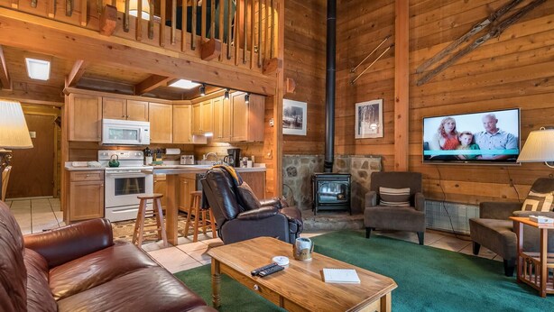 Interior acogedor de una cabaña con detalles de madera, una cocina, chimenea y televisor.