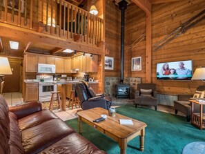 Un intérieur de chalet chaleureux, avec un revêtement en bois, un coin cuisine, une cheminée et un téléviseur.