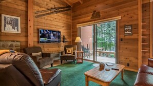 Interior acogedor de una cabaña con detalles de madera, muebles de cuero, un televisor y un ventanal con vista a una terraza.