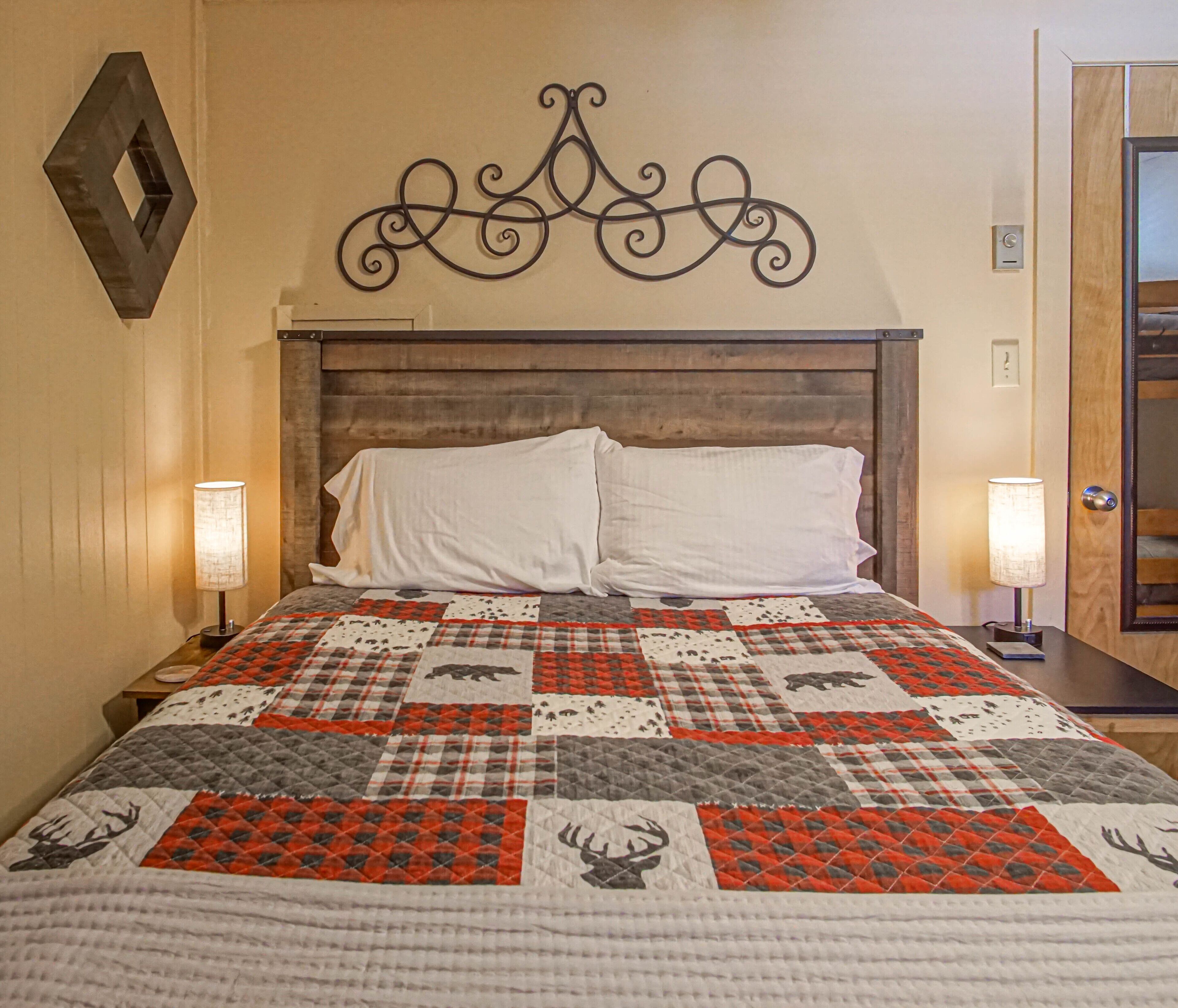 A bed with a quilt featuring animal patterns, a wooden headboard, two bedside lamps, and a door to the right.