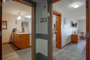 Uma cozinha moderna com armários de madeira e uma ilha central, um corredor com porta de madeira e uma sala de jantar com mesa e cadeiras.