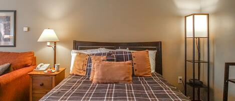 A hotel room with a bed, a nightstand, a lamp, a telephone, and a framed picture on the wall.