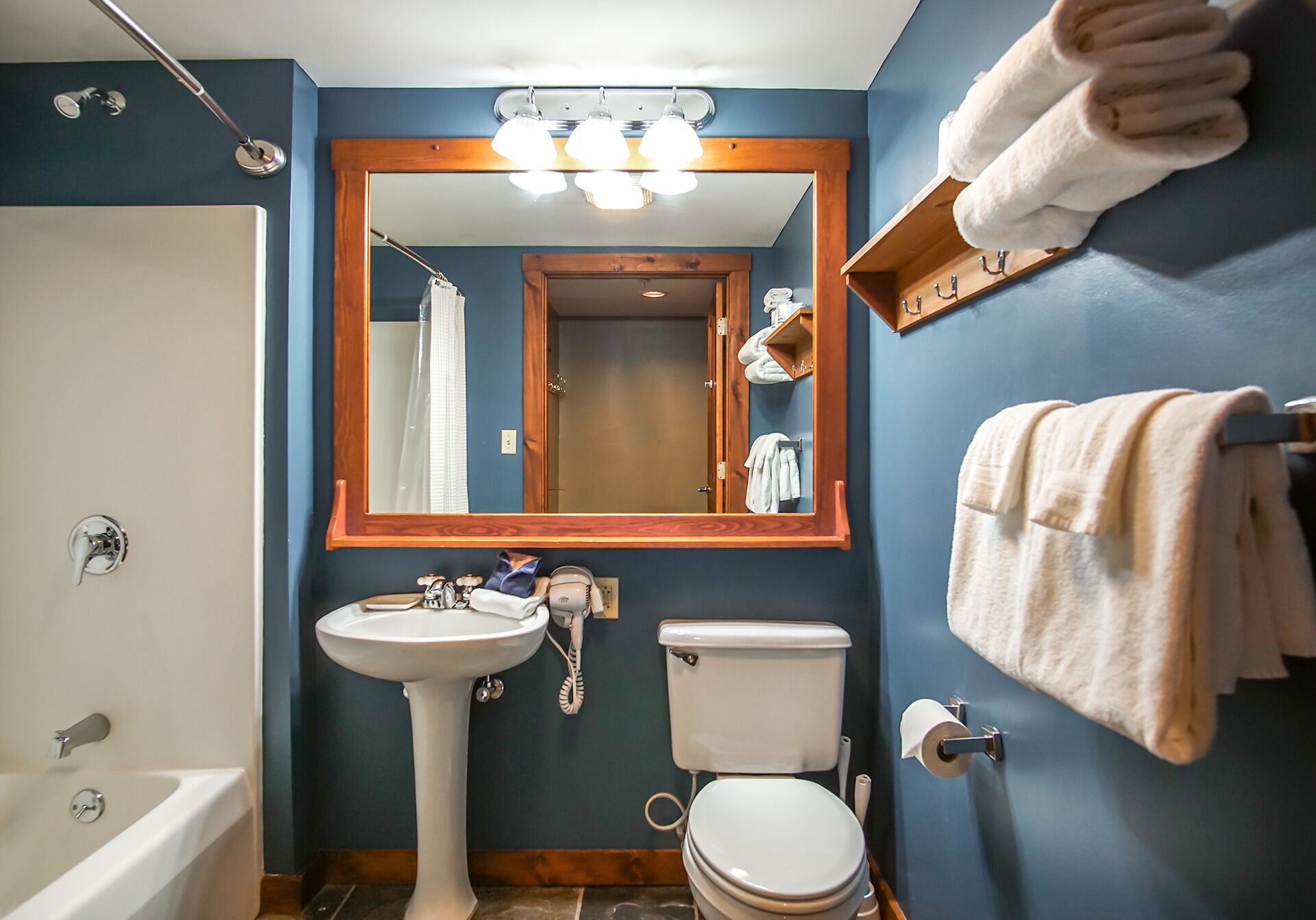 Baño con bañera, lavabo, inodoro y espejo con luces arriba.