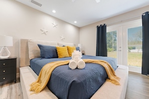 Un dormitorio con cama, mesita de noche, lámpara y vistas al exterior.
