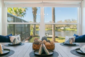 A dining table with a basket of decorative items and a view of a lake and trees through large windows.
