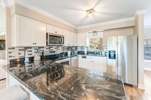A modern kitchen with white cabinets, a black marble countertop, stainless steel appliances, and a built-in microwave.