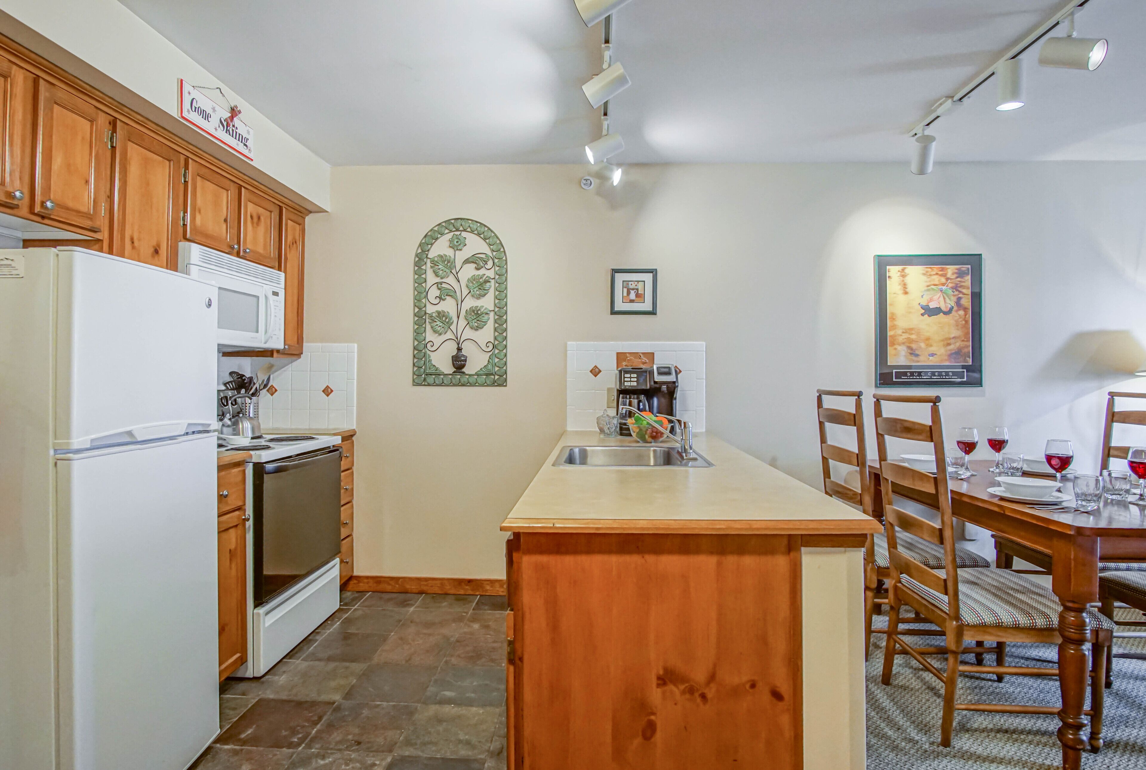 A kitchen with wooden cabinets, a white refrigerator, a microwave, a sink, and a dining area with a wooden table and chairs.