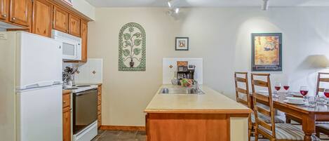 A kitchen with wooden cabinets, a white refrigerator, a microwave, a sink, and a dining area with a wooden table and chairs.