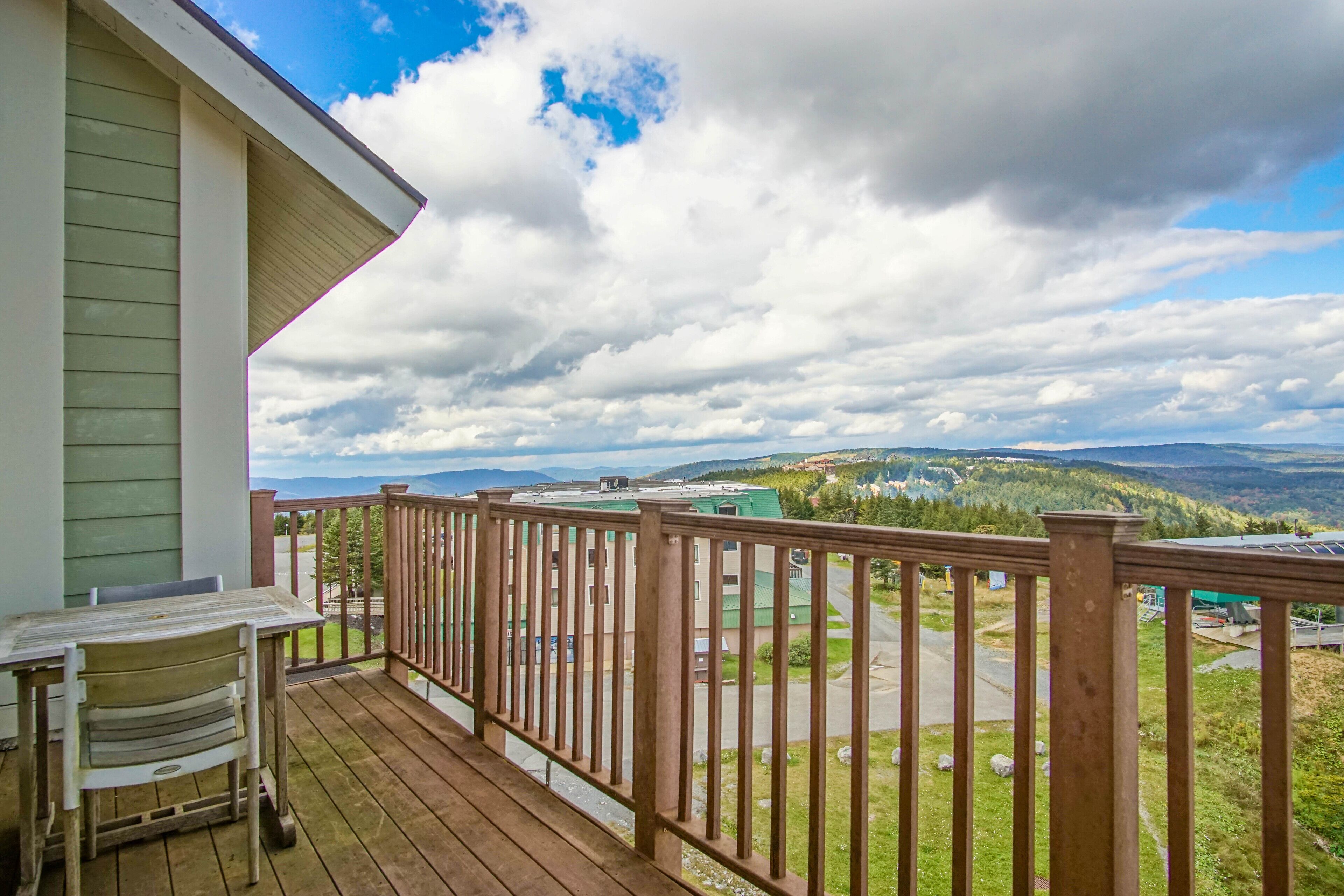 A wooden deck with a view of a green landscape and distant mountains.