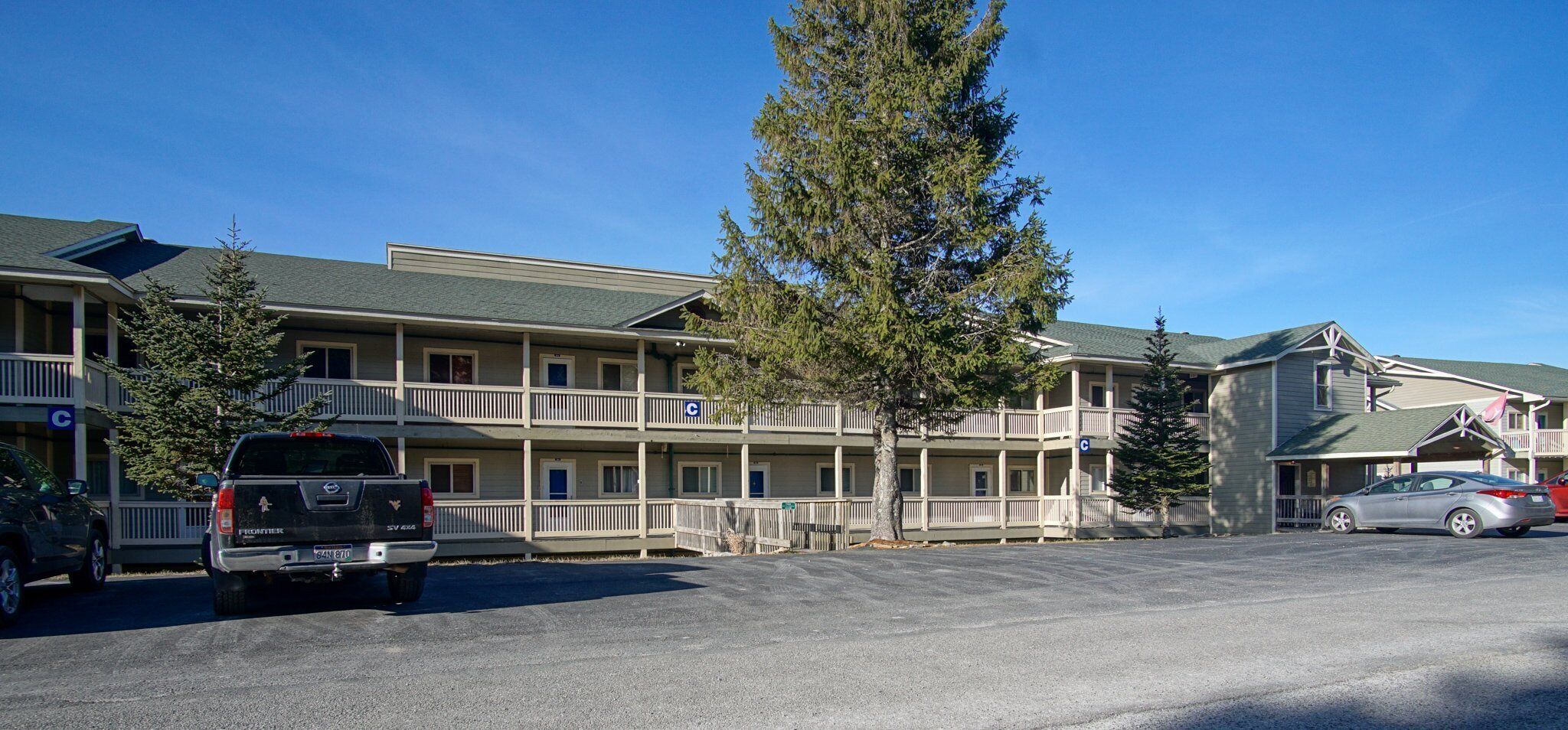 Un motel con diversi balconi, un parcheggio e alcuni veicoli parcheggiati di fronte.
