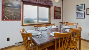 Ein Esszimmer mit großem Fenster, Holztisch und Stühlen. An den Wänden befinden sich gerahmte Bilder.