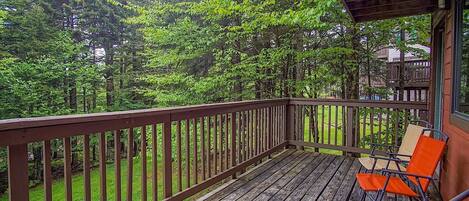 A wooden deck with a railing, surrounded by dense green trees.