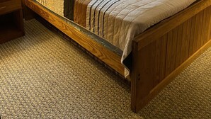 Una cama con estructura de madera, colcha a rayas, dos almohadas y una mesita de noche.