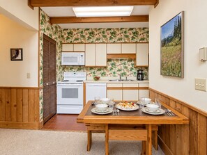A compact kitchen with wooden cabinets, a microwave, a stove, and a dining table set for two. - Whistlepunk 40 Bavaria`s Finest-1 Bedroom With Loft, Slope Side (Snowshoe)