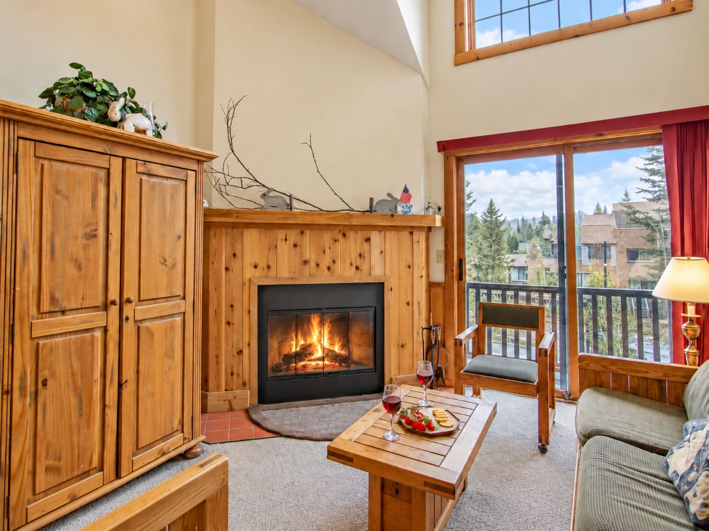 A cozy living room with a fireplace, wooden furniture, and a balcony with a view.