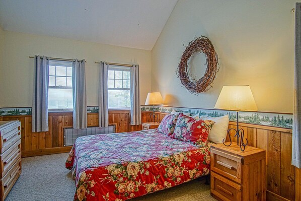 Un dormitorio con cama, dos mesitas de noche, lámpara de pared y ventana con cortinas, además de un adorno decorativo.