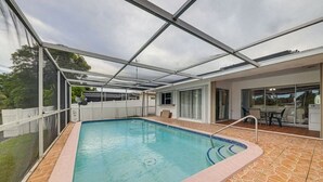 En overdækket swimmingpool med glasloft, omgivet af en terrasse med udendørs møbler.