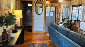 A cozy living room with a blue sofa, wooden flooring, a dining area with a table and chairs, and a kitchen visible through an open door. - Stargazer Cabin: Sauna, Rooftop Deck, Fire Pit, Indoor Wood Fireplace, Privacy (Blue Ridge)